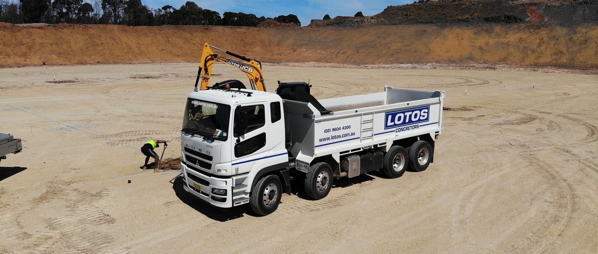A company-owned Lotos tipper truck and excavator on a bulk earthworks site