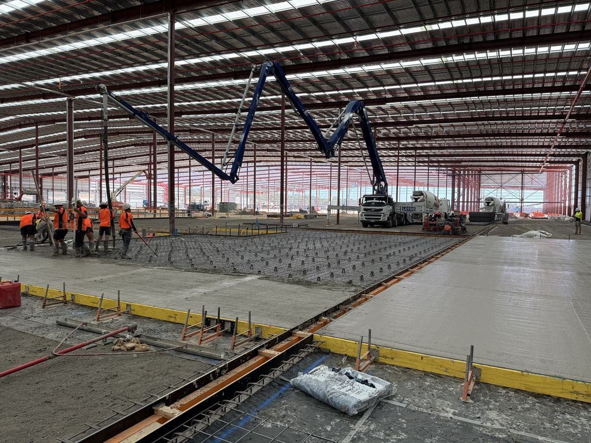 A Lotos boom pump and crew placing concrete inside a steel-framed warehouse