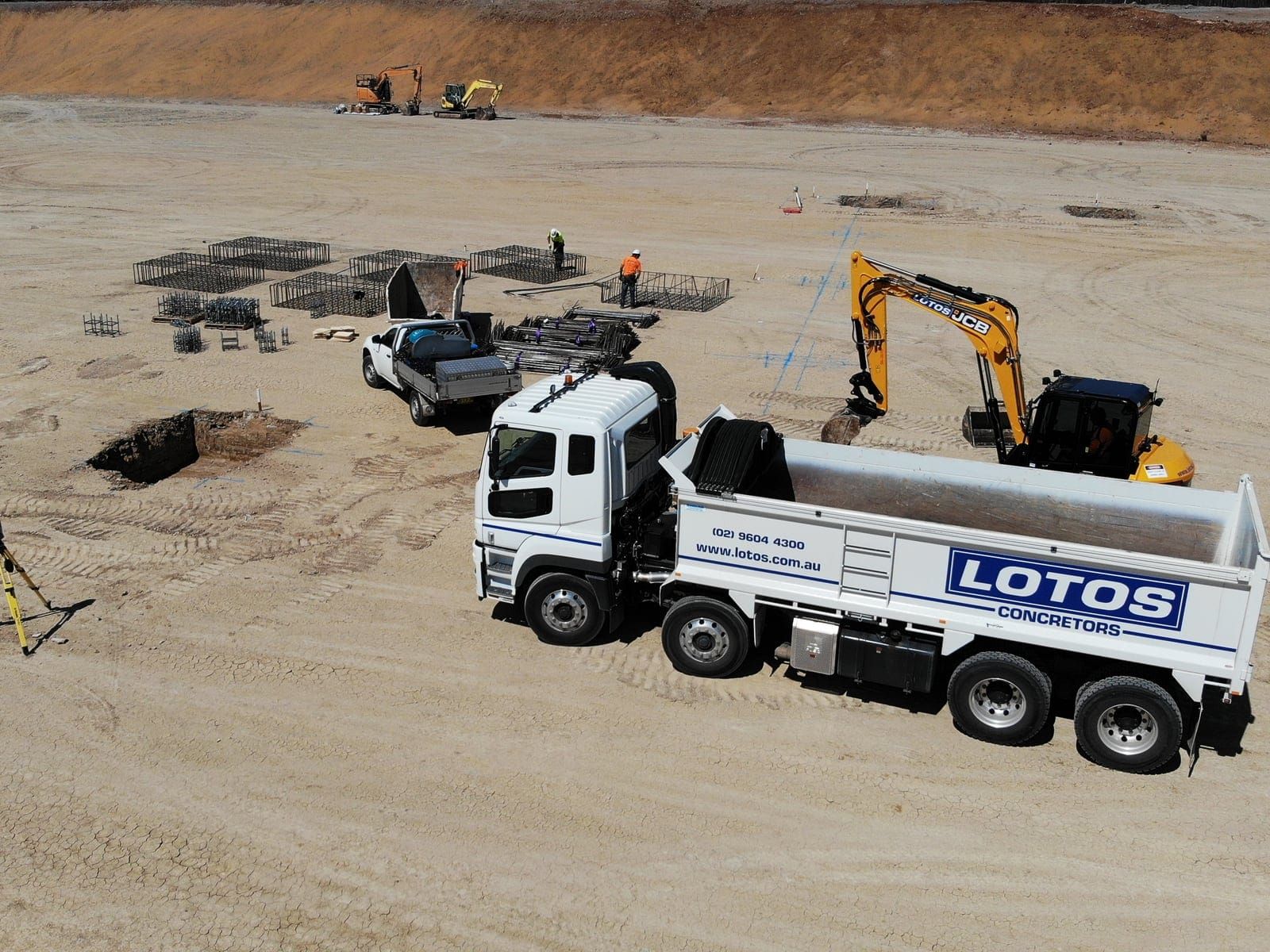 A Lotos Concretors tipper truck and tracked excavator on a prepared pad, with pile cages set out