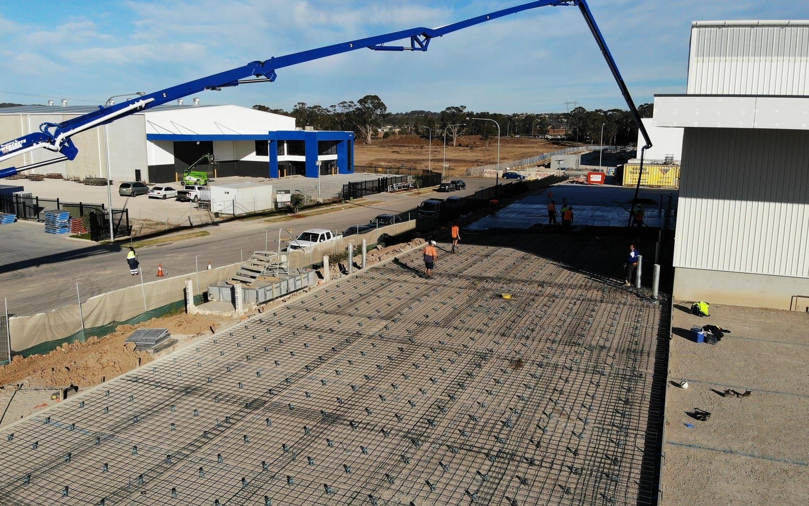 A Lotos boom pump reaching over a reinforced slab bay beside a completed warehouse