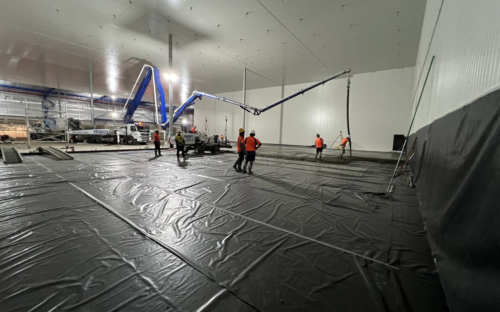 A boom pump and crew placing a wearing slab inside a freezer chamber